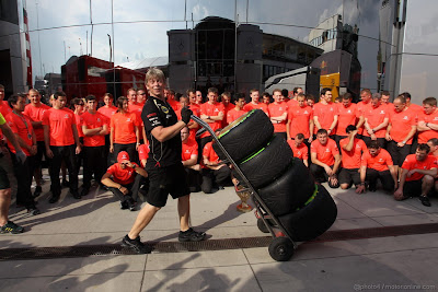 механик Lotus провозит резину Pirelli перед групповой фотографией McLaren на Гран-при Венгрии 2012