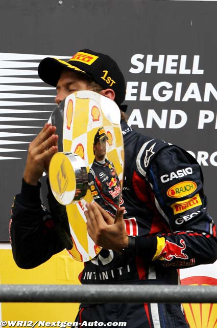 Себастьян Феттель целует трофей в отражении которого Марк Уэббер на подиуме Гран-при Бельгии 2011