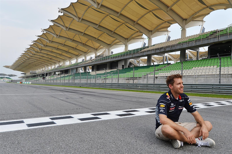 Себастьян Феттель сидит на старт-финишной черте трассы Куала-Лумпур на Гран-при Малайзии 2013