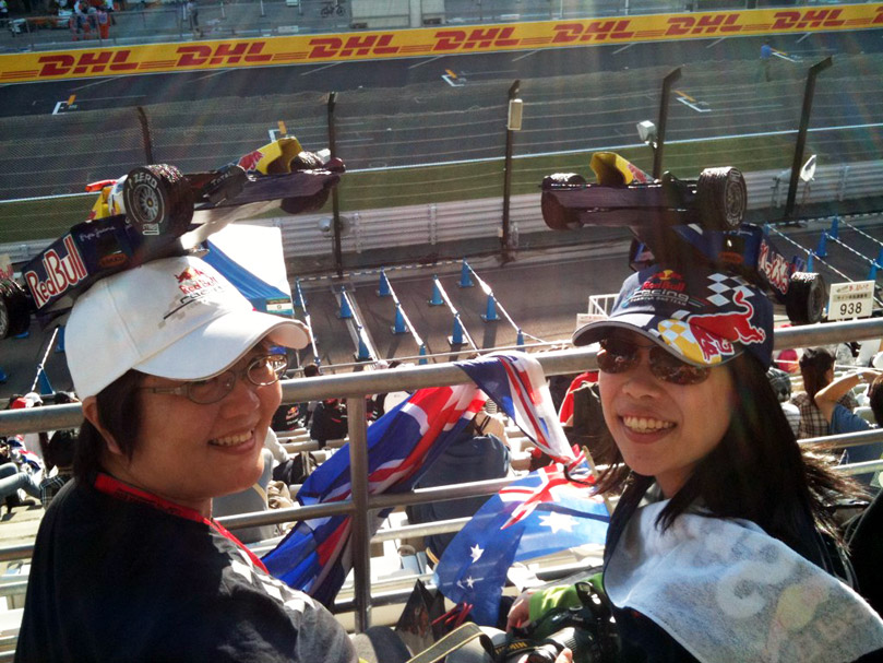 болельщиы Red Bull в кепках с болидами на трибунах Сузуки на Гран-при Японии 2011