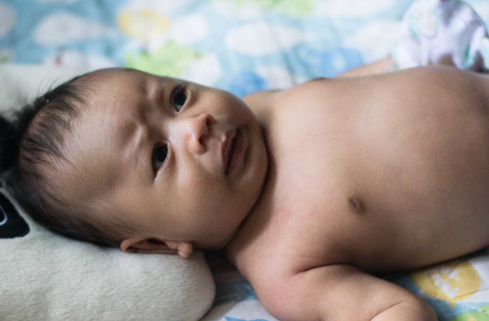 baby focusing eyes on an object off-screen on bright blue and white blanket