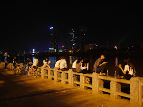 people sitting on a stone railing next to the Xiang River at night