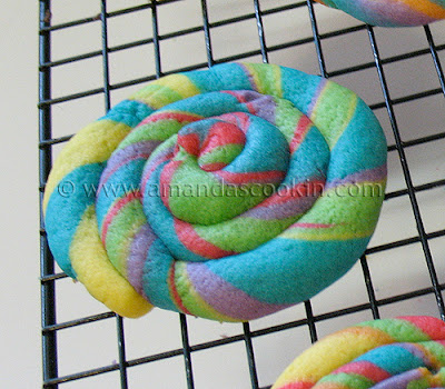 A photo of rainbow cookie in the shape of a coil resting on a wire cooling rack.