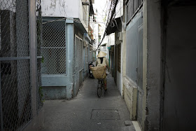 woman wearing a nón lá (leaf hat) and riding a bicycle through a narrow alley