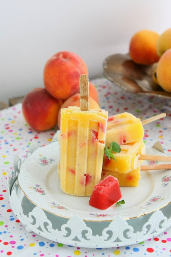 Strawberry and peach popsicles with a pile of fresh peaches in the background