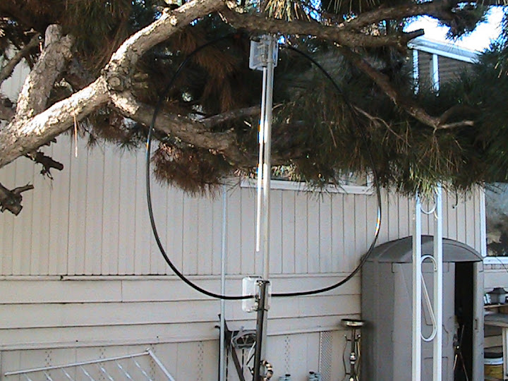 The
                      magnetic loop antenna assembled on a 5 foot length
                      of 1/2 inch PVC conduit and mounted on a tripod.
                      The 112 inch loop of RG-8A/U coaxial cable is
                      attached to the SO-239's on the tuning enclosure.
                      The transmission line is RG-58/U coaxial cable
                      with 2 turns threaded through ferrite cores at the
                      feed point to form a choke balun. The capacitor is
                      adjusted using a vinyl mini-blind wand attached to
                      the shaft of the reduction drive with a small hose
                      clamp.