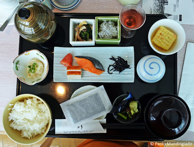 Japanese breakfast set (clockwise from center): roe, smoked tofu, salmon, seaweed, mushrooms with eggs and veggies, small fry, palate cleanser (sweet wine, perhaps), tamago, pickled plum, miso soup, picled veggies, nori sheets, rice, raw squid strips, and silken tofu. Some of the items in this tray I barely recognized. :-P