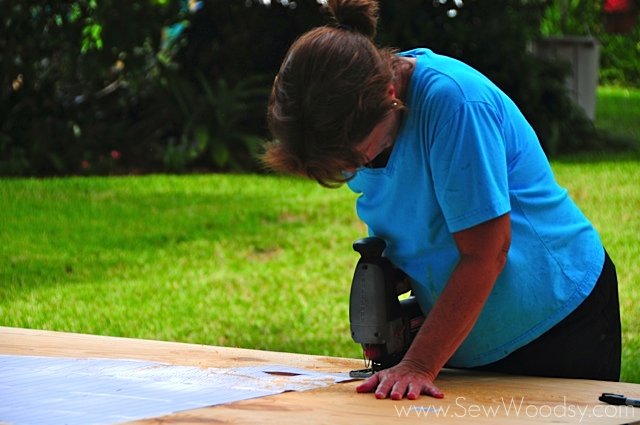 Woman using a jigsaw cutting around a paper template on plywood.