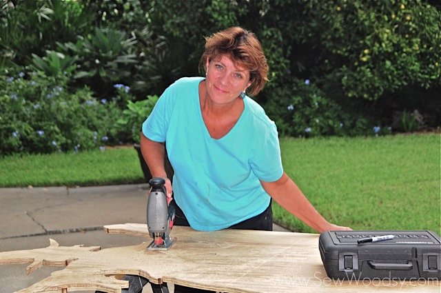 Woman smiling cutting with a jigsaw on plywood.