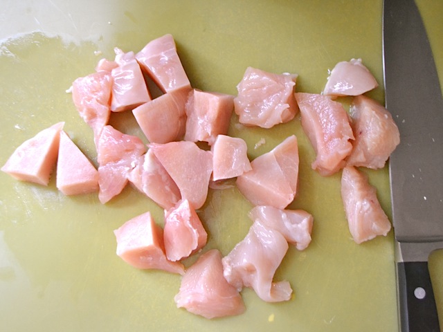 raw chicken cut into small chunks with knife 