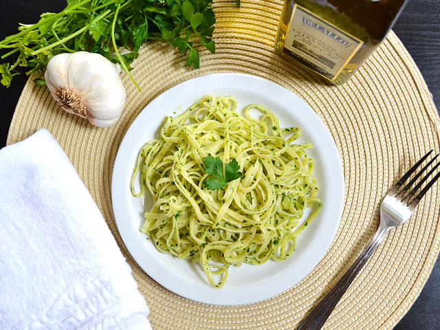 Top view of a plate of Parsley Pesto Pasta with fork, napkin, olive oil and garlic staged on the side