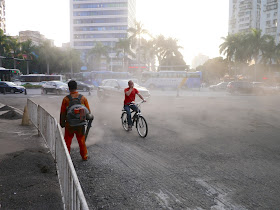 man covering his mouth with his hand while riding a bike through a dust cloud created by a gravelblower