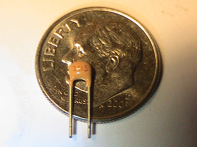 One
                    of the kit's 0.01 μF monolithic capacitors. Having
                    built a Heathkit HW-101 in the 1970's and most
                    recently a Heathkit SB-1000 amplifier in the 1990's,
                    this was my first kit that required using a
                    magnifying lens to identify the component values.
                    Confirming the value of each of these little
                    components and finding its mounting holes on the
                    printed circuit board reminded me of the times I've
                    played the old "Where's Waldo?" game over
                    and over!