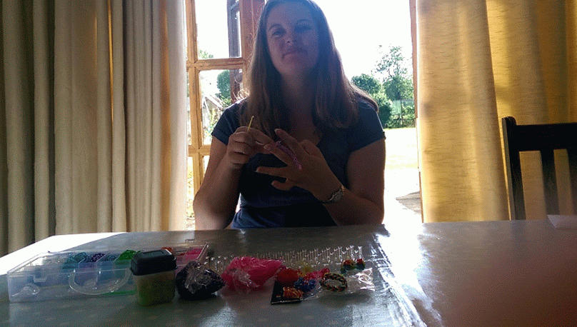A woman sitting at a table in front of a window using loom bands