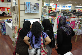 4 girls, 3 wearing a hajib, looking at a computer screen in a bookstore