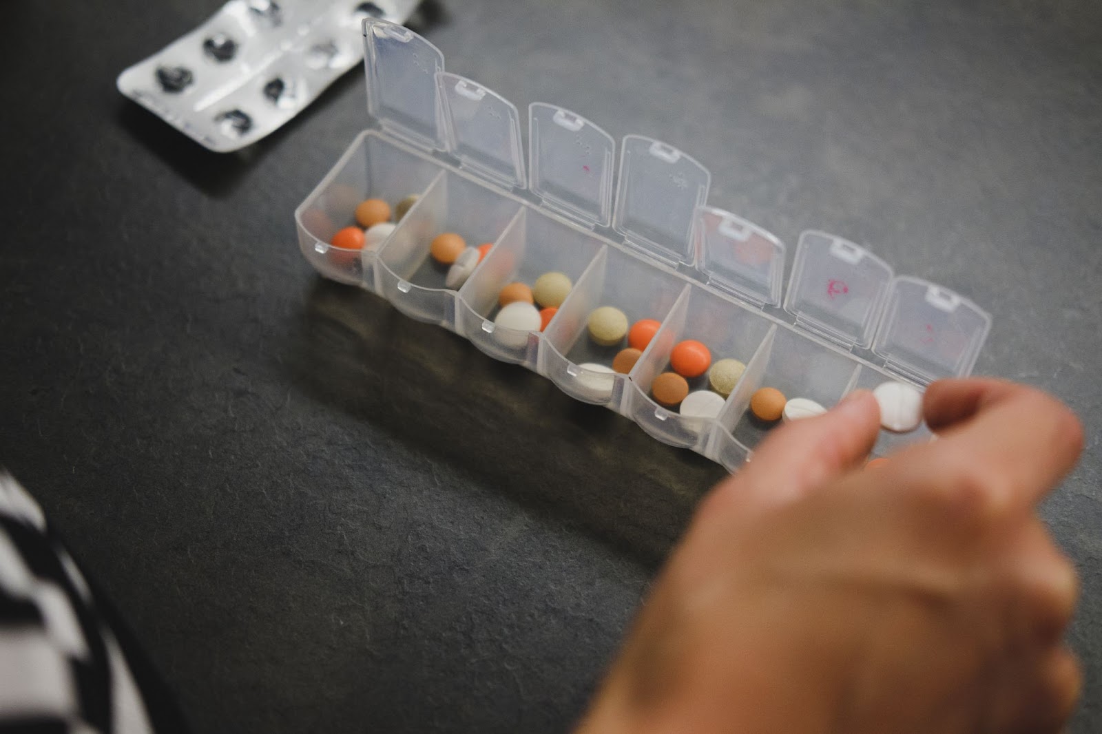 someone putting a pill into a plastic pill box
