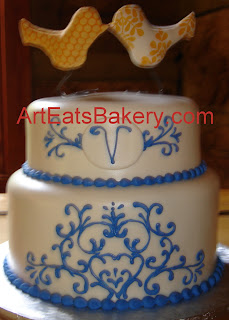 Two tier white fondant wedding cake with custom cornflower blue piping design and monogram and bird topper