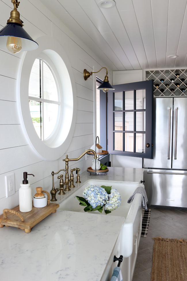 white farmhouse kitchen with shiplap walls, brass faucet hardware, white marble countertops and matte black hardware