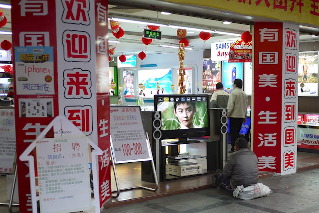 man sitting on a sack while watching a TV at a store