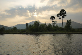 mountains, tropical trees, and a river with a setting sun