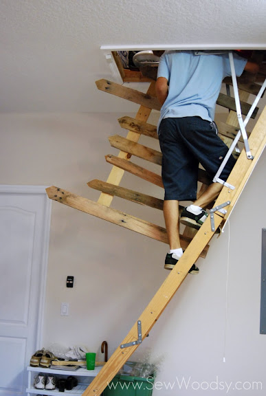 Man standing on stairs in garage trying to put a fence in the attic.