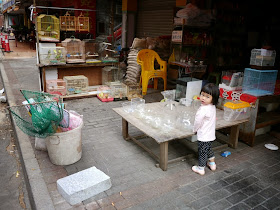 little girl looking at me while she stands at a low table with fishbowls in front of a pet store
