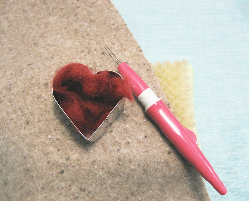 Lay felted fabric on top of the felting pad. Place cookie cutter in desired area, and fill with loose roving. Lay felted fabric on top of the felting pad. Place cookie cutter in desired area, and fill with loose roving.