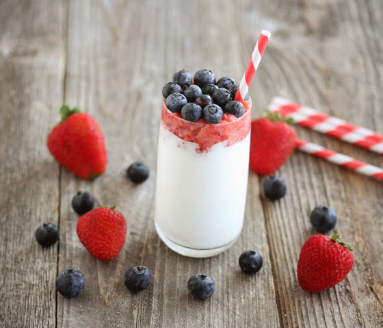 one Red White and Blue Milkshake with a red striped straw and fresh berries around the glass