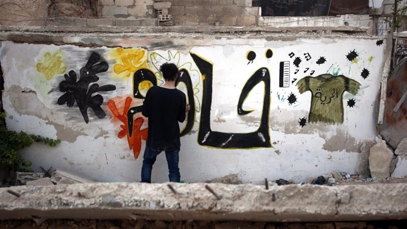 Syrian artist Noor paints graffiti that says 'Resist' on a destroyed wall in rebel-held al-Qaboon neighbourhood, in outskirts of Damascus, [EPA]