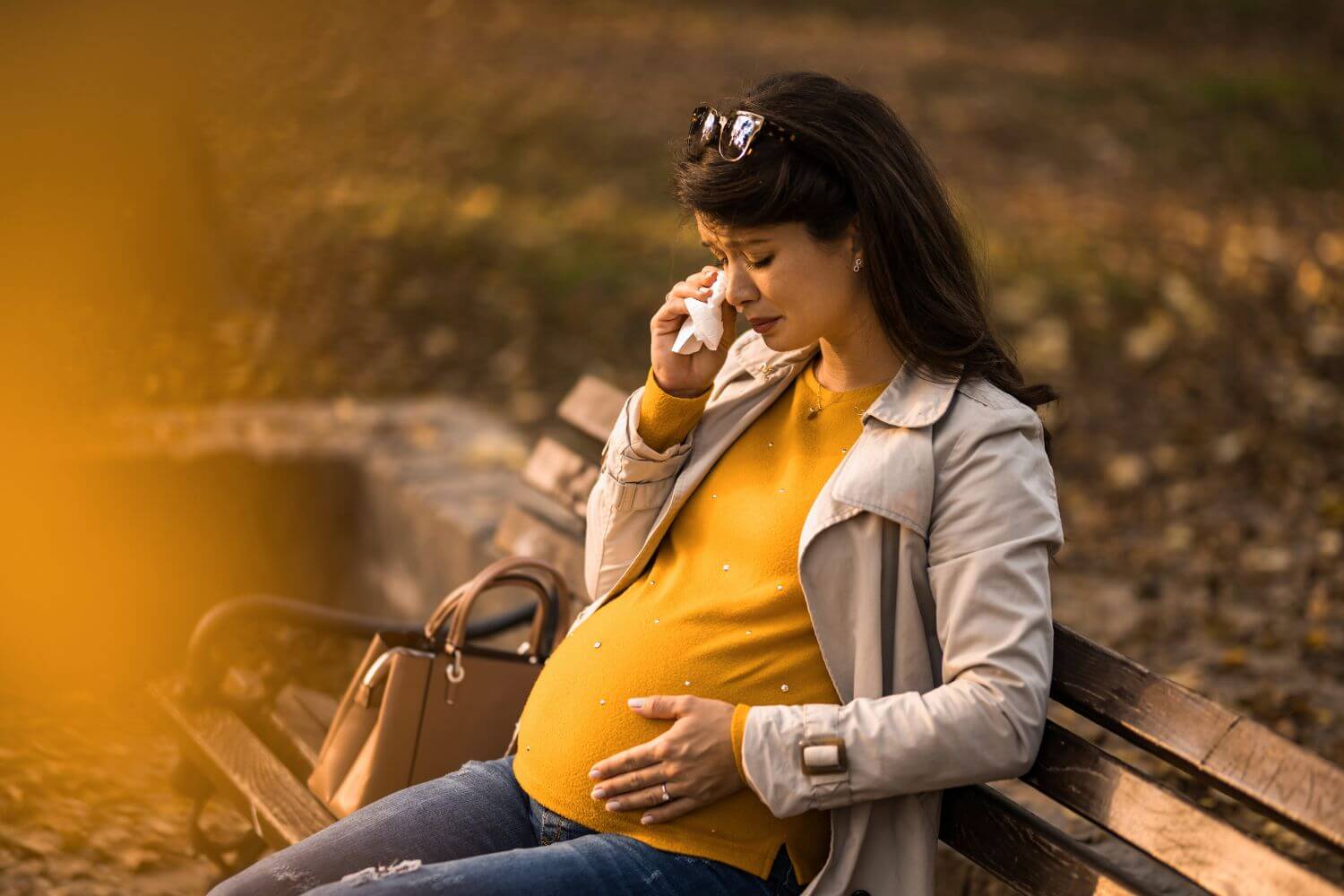 Pregnant woman sitting on a bench outside, crying