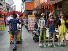 man pushing a food stall past mannequins in Yangjiang, China
