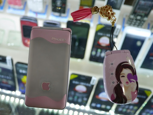 an iPoone flip phone with a partial Apple logo and a small pink flip phone with a drawing of a young woman holding a heart