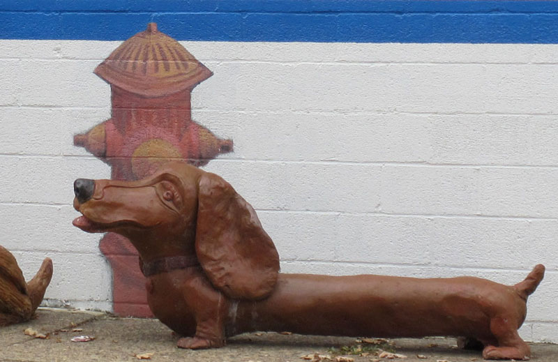 Fire hydrant mural on wall behind dachshund sculpture.