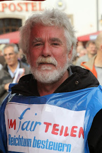 Demonstrant mit umgehängtem Transparent: »umfairteilen – Reichtum besteuern«.