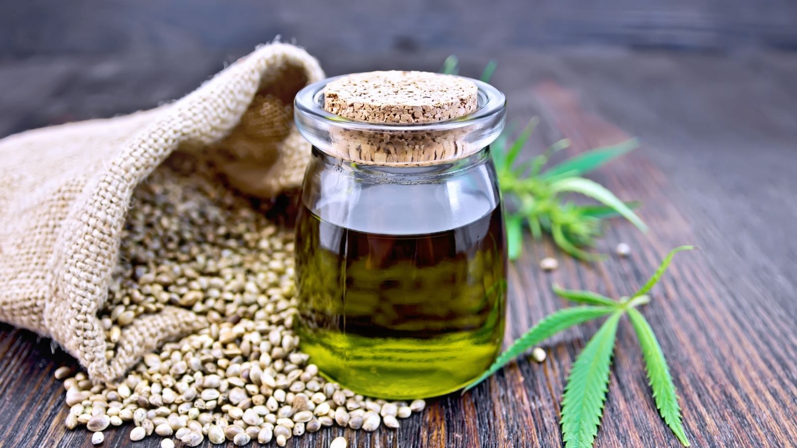 Jar of cannabis oil displayed with hempseeds and cannabis leaf.
