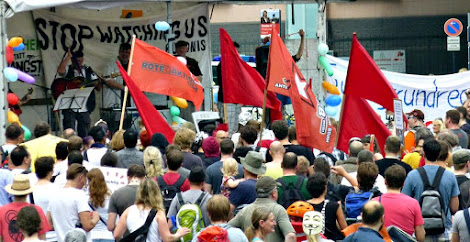 Tribüne, zahlreiche Demonstranten, rote Fahnen.