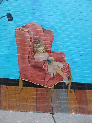 Little girl reading in a pink wing back chair.