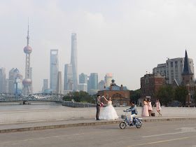 posing for wedding photos with Shanghai skyscrapers in the background and a woman on an electric bike passing in front