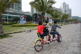 three people riding a triple tandem bicycle and an artistic display of bicycle riders nearby in Zhuhai, China