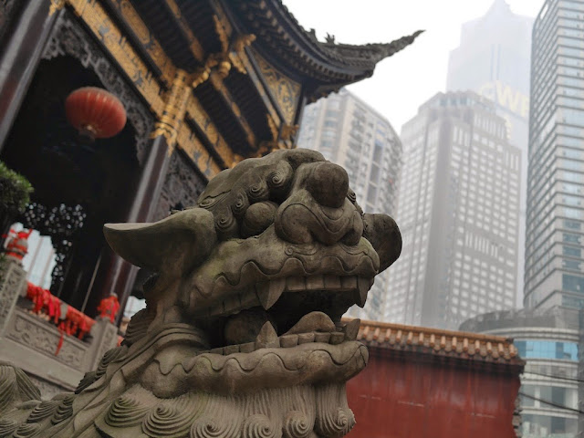 Chinese guardian lion in front of a temple with tall office buildings in the background