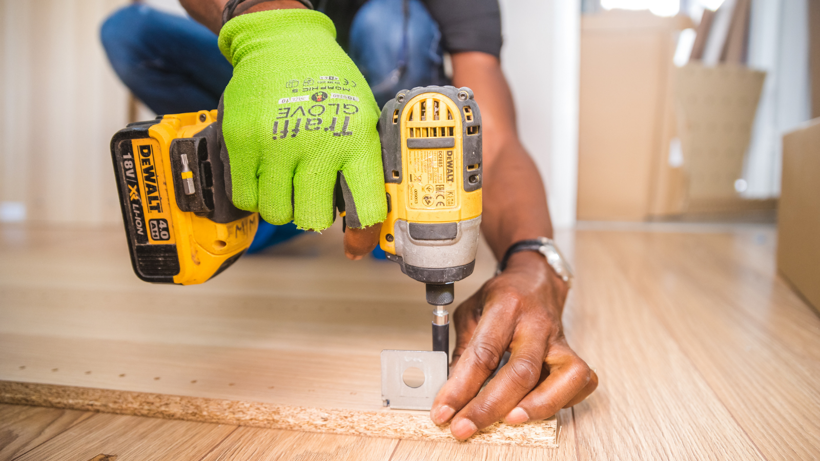 Gloved hand holding drill against a piece of wood