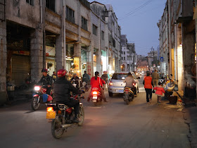 motorbikes, a car, and pedestrians in an evening road scene in Yangjiang, China