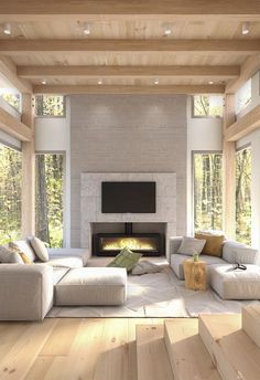 A cozy living room with large windows, a modern fireplace, a wall-mounted TV, and a light-colored sectional sofa with accent pillows, creating a warm and inviting space surrounded by natural light.