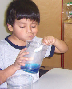 Child tries to move water from a tall container using a spoon.