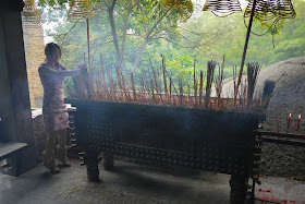 Young woman placing incense sticks at a temple in Bailian Dong park in Zhuhai China