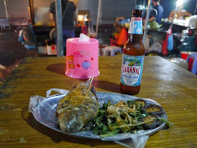 a bottle of Saranac White IPA next to a plate with grilled fish and vegetables on an outdoor table