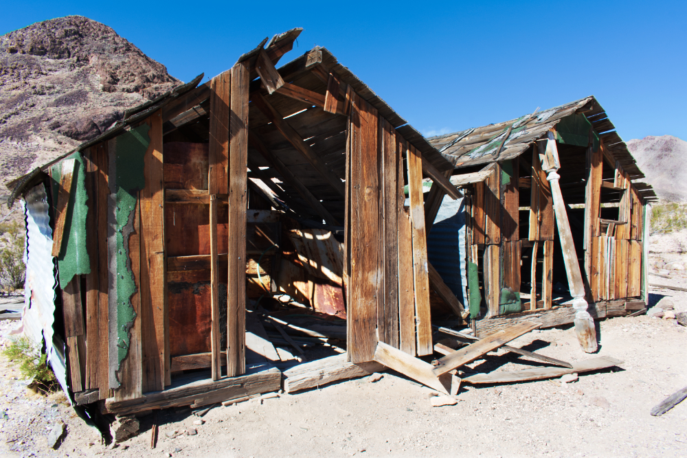 Two abounded sheds in the desert with mountains in the distance. 