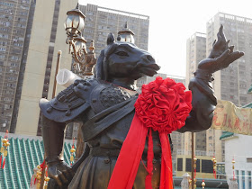 statue of a human figure with a horses head in traditional Chinese armor holding a flame