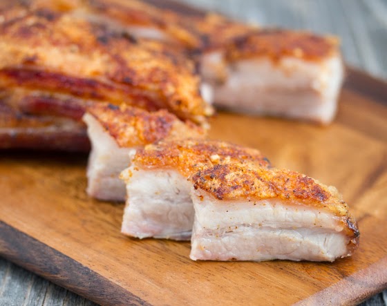 a close-up of three slices of crispy pork belly lined up on a cutting board