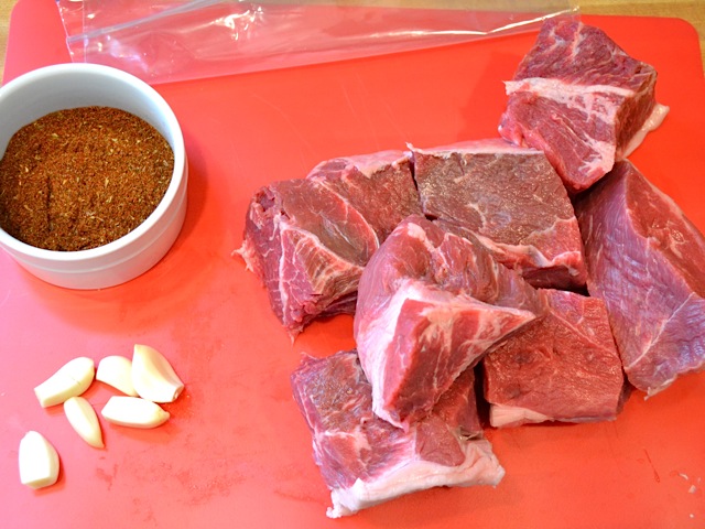 beef cut into chunks with bowl of spice mix next to them 